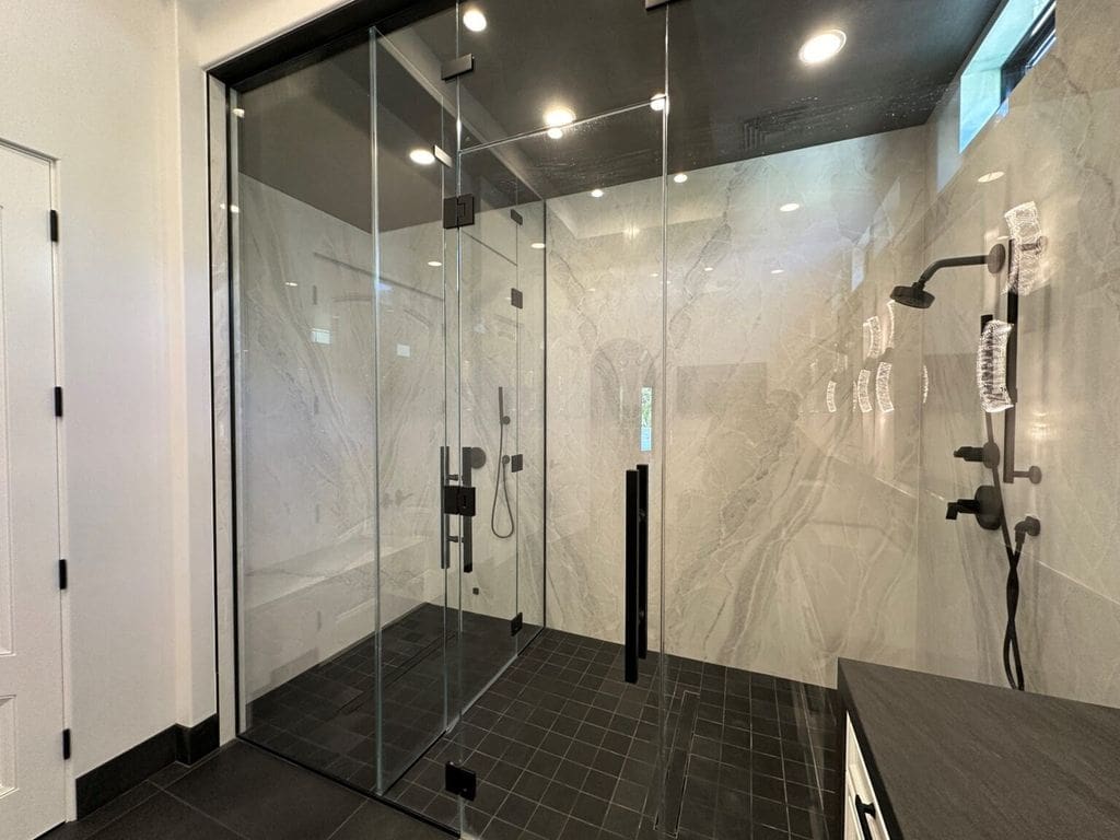 A bathroom with a glass shower door and black tile floor.