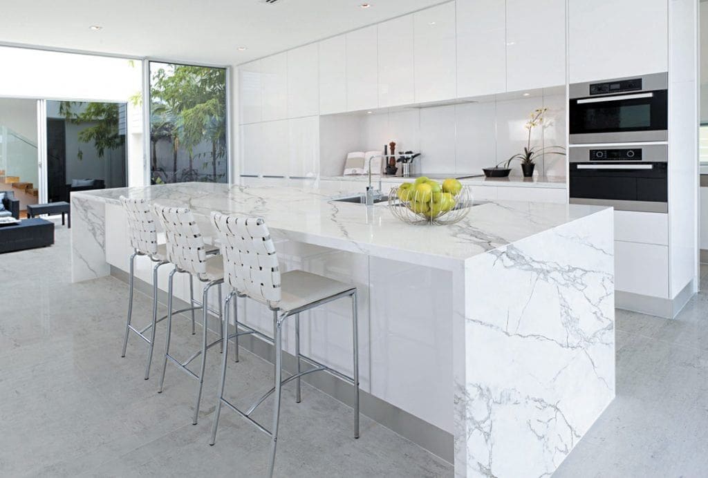 A kitchen with marble counter tops and white cabinets.