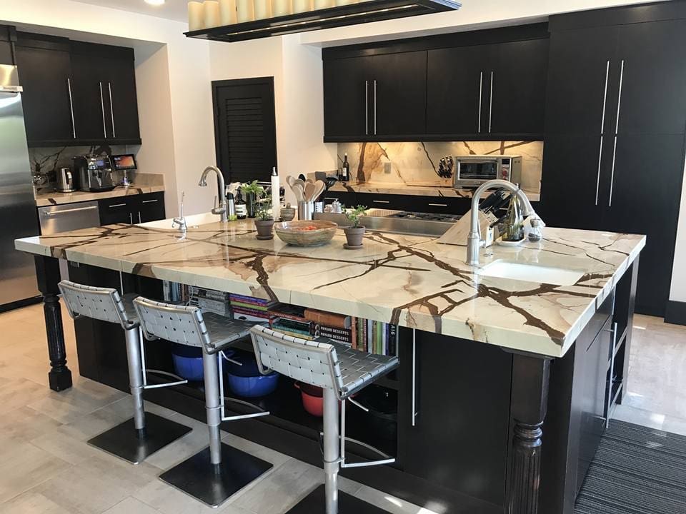 A kitchen with marble counter tops and black cabinets.