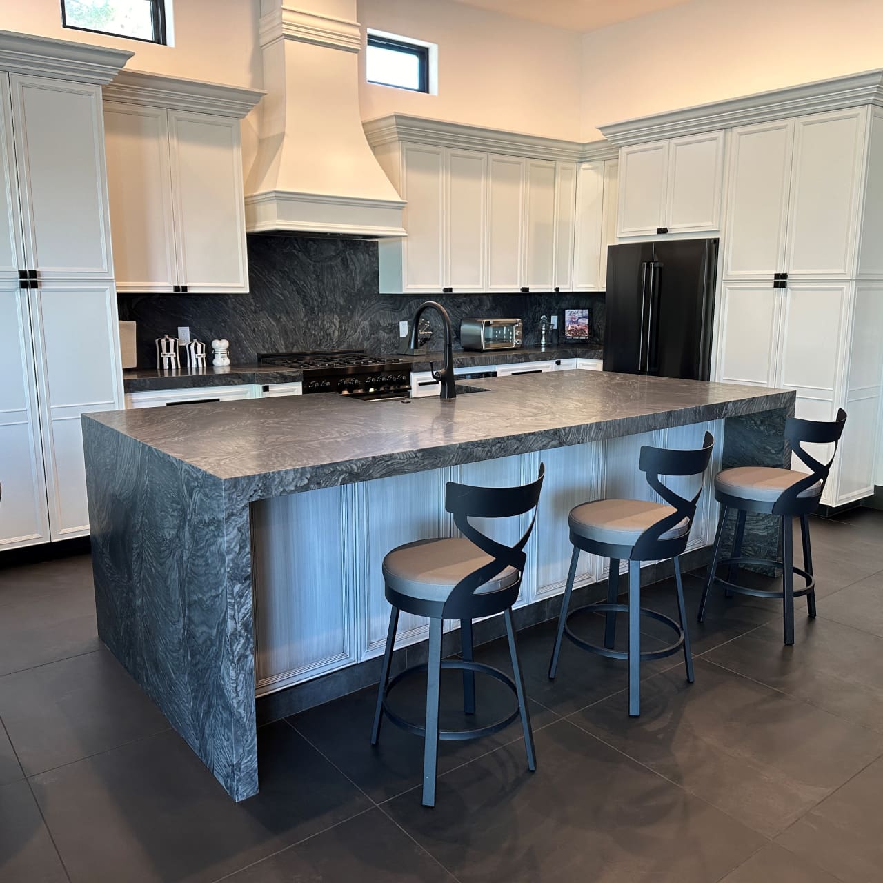 A kitchen with a large island and black stools.